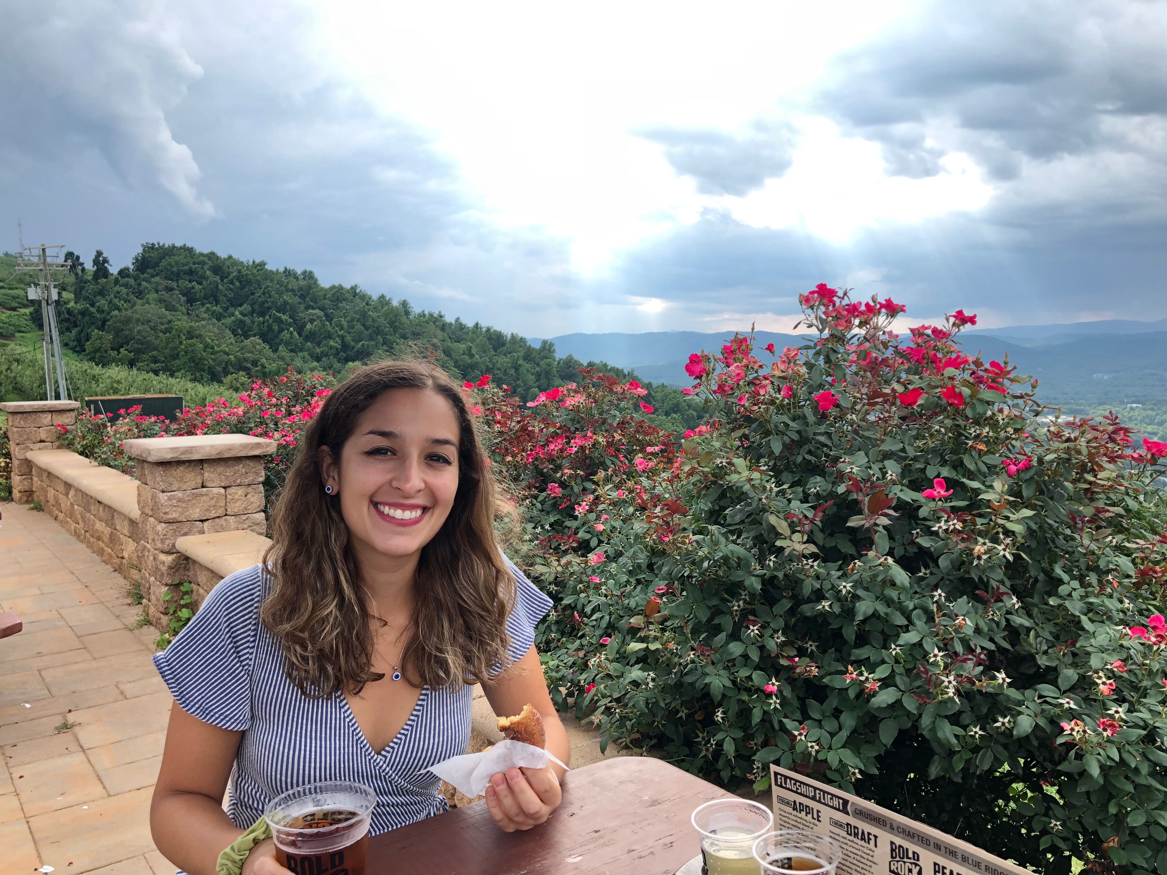 Woman savoring cider and enjoying an apple cider donut at Bold Rock Cidery, Carter Mountain, with a backdrop of scenic mountains on her Shenandoah National Park Itinerary.