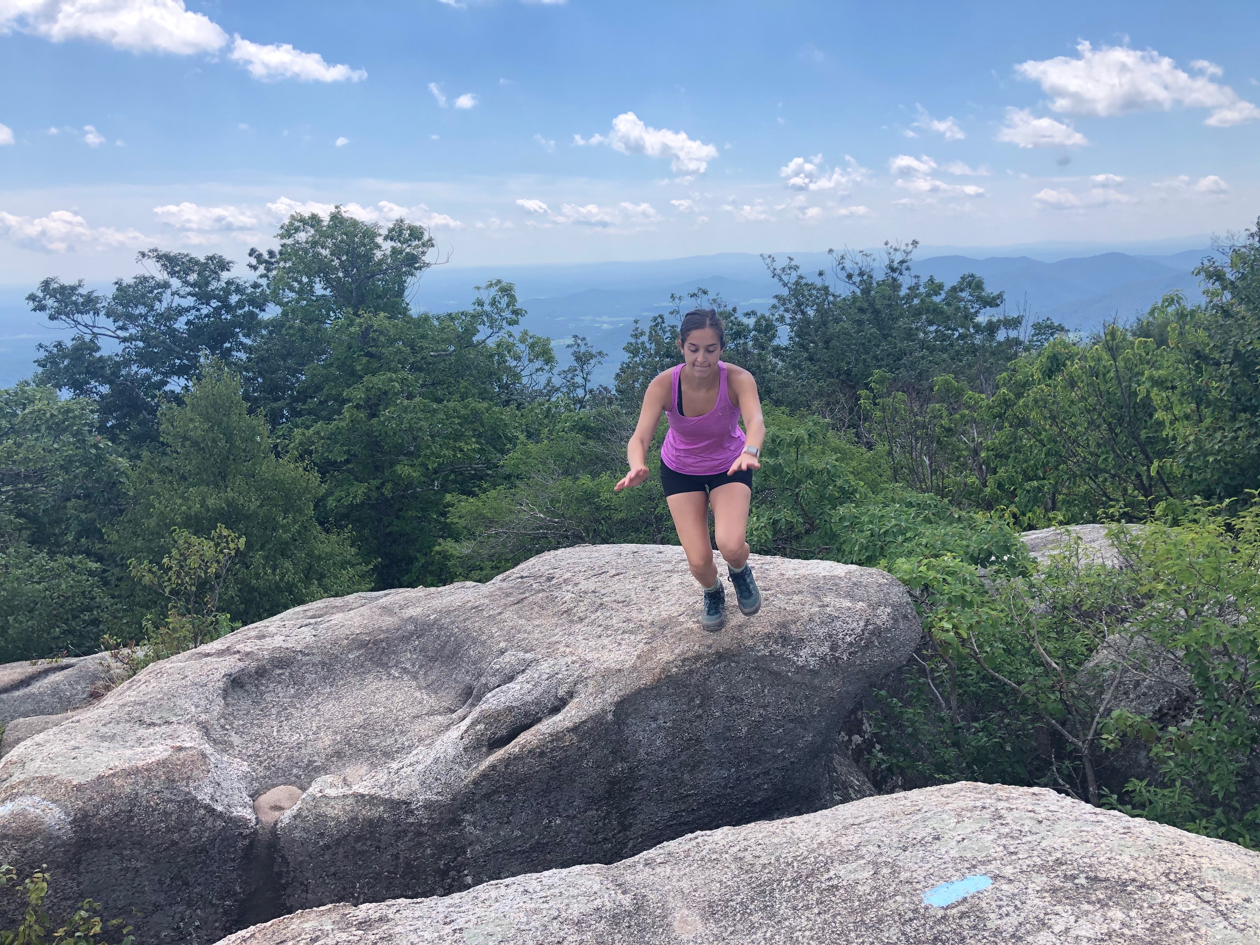 Adventurous woman hiking Old Rag Mountain, skillfully leaping from one rocky outcrop to another, surrounded by the scenic beauty of the trail and the natural landscape