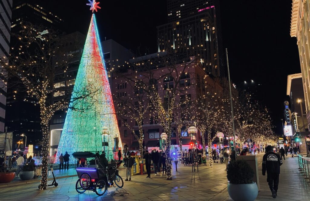 16th Street in Downtown Denver at night. Trees line the streets with Christmas lights and a large light up Christmas tree. Visiting Denver in one day has to include this pedestrian street. 