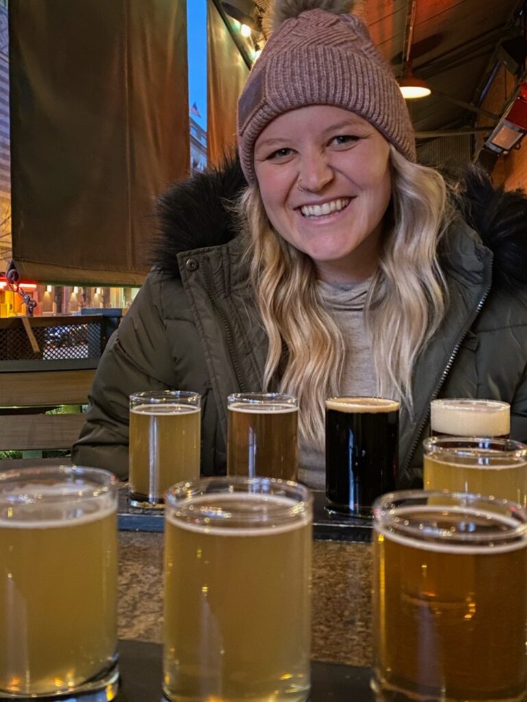 Madi (author) sitting at Wynkoop Brewery with a flight of beer in front of her. 