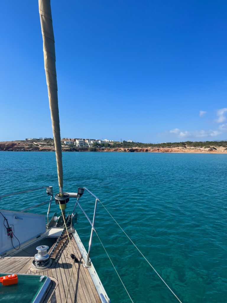 Serenity on the Aegean Sea: A tranquil scene from a sailboat, showcasing the crystal-clear waters of the Aegean. In the background, a picturesque Greek island emerges, adorned with rocky cliffs and vibrant greenery, inviting a sense of peaceful exploration and Mediterranean beauty