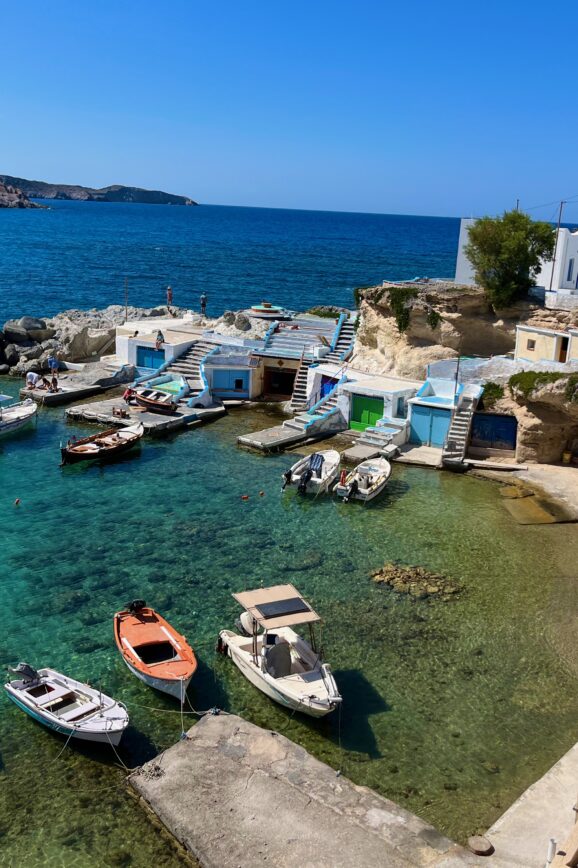 Idyllic coastal scene in Mandrakia, Milos, Greece, featuring traditional fishing boats gently bobbing in the crystal-clear turquoise waters. Mandrakia is a MUST on your Milos Itinerary.