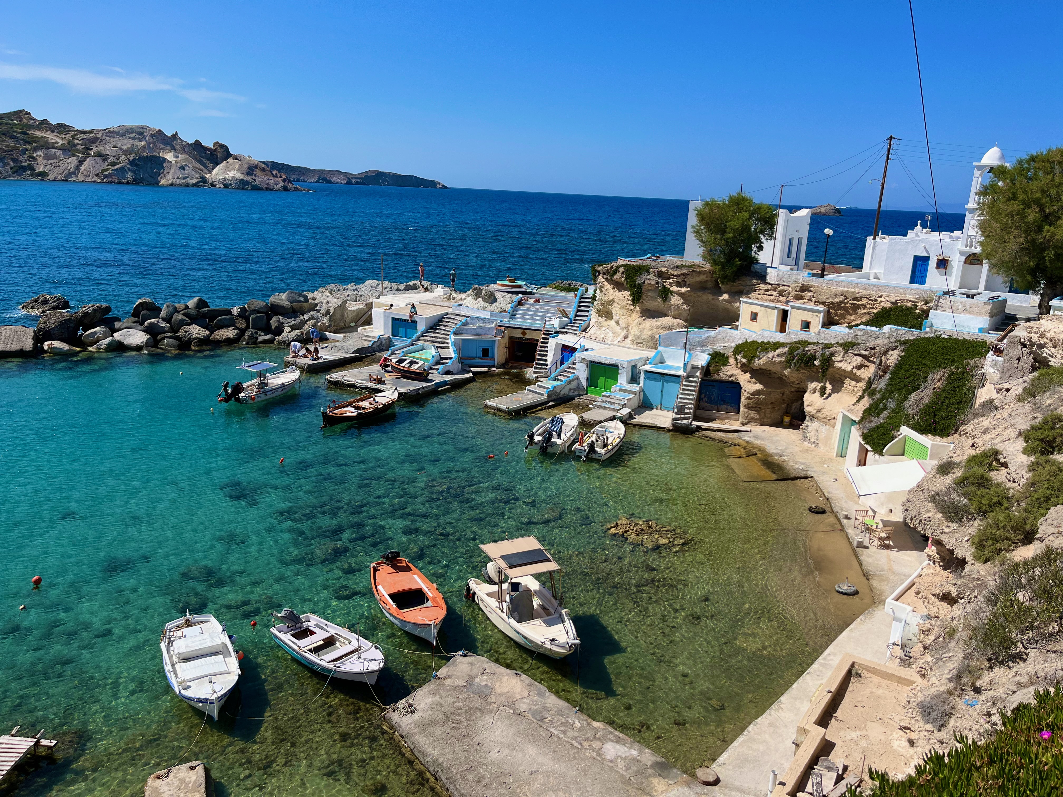 Idyllic coastal scene in Mandrakia, Milos, Greece, featuring traditional fishing boats gently bobbing in the crystal-clear turquoise waters. Mandrakia is a MUST on your Milos Itinerary.