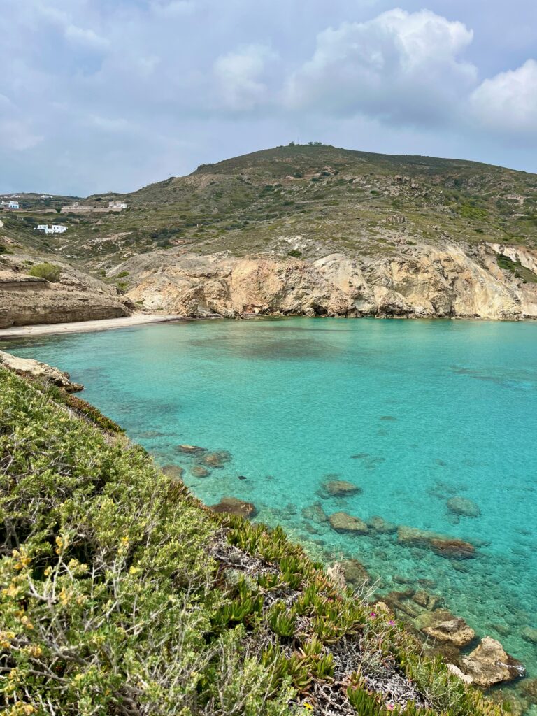 Idyllic view of the sun-kissed beach in Mandrakia, Milos, Greece, where turquoise waters meet the pebbled shore, surrounded by quaint fishing cottages, embodying the tranquil beauty of the Aegean coastline