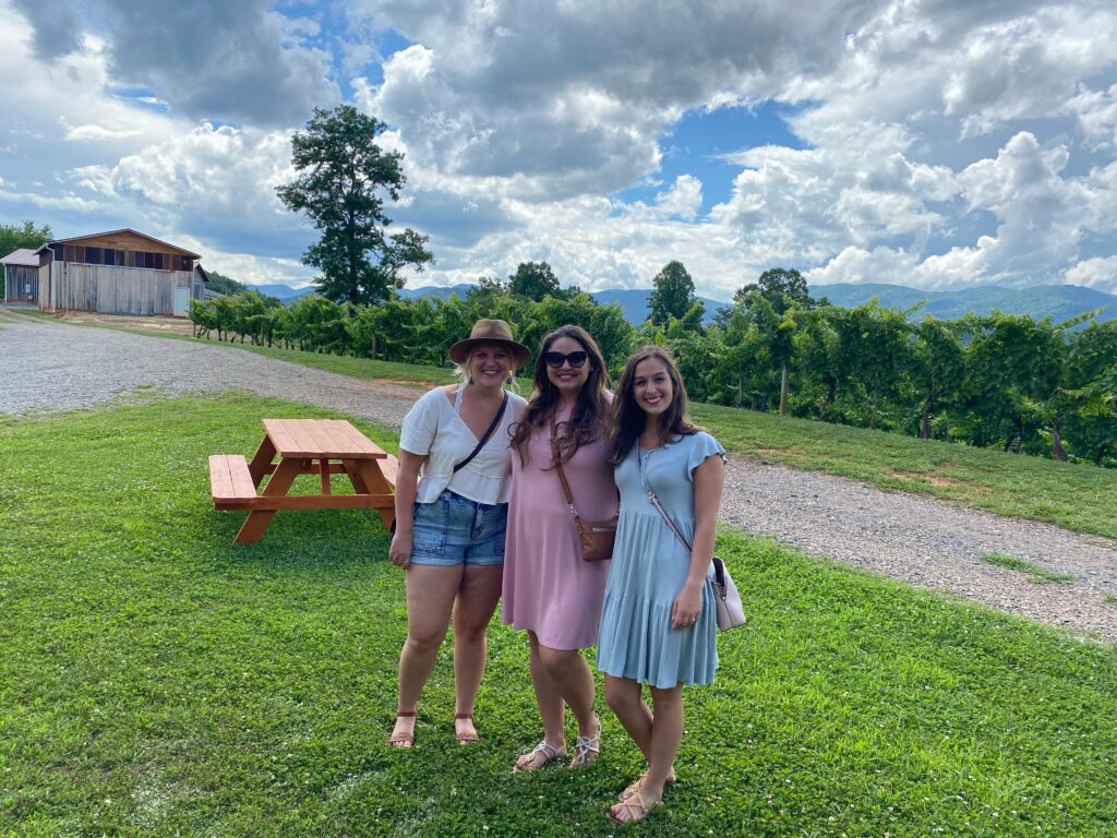 Three girls in front of a mountain landscape on their Asheville bachelorette party winery trip.